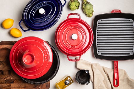 selection of red and blue Staub cast iron cookware with asparagus, lemon, and oil dispenser